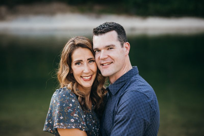 Dr. Trevor Griffitts, DMD, smiling alongside his wife in a close portrait with a blurred natural water background.